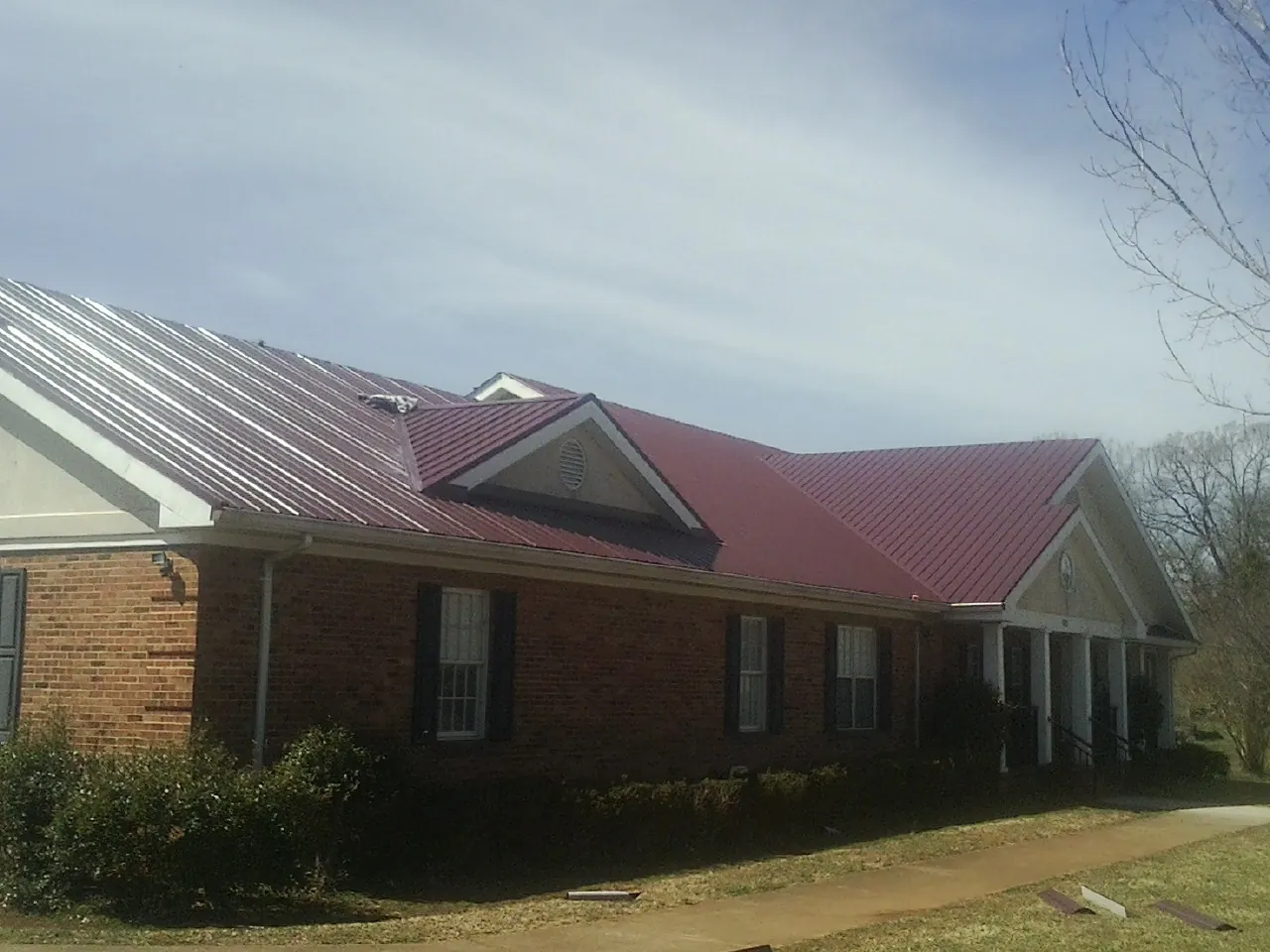 Red metal roof with gabled entries on a long brick building, from a Hail Damage Roof Repair job in Rhodesdale