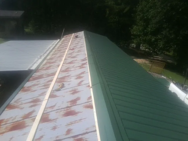 Old rusted panels beside newly installed green metal roofing — Wind Damage Roof Repair by Roofing Brothers in Rhodesdale