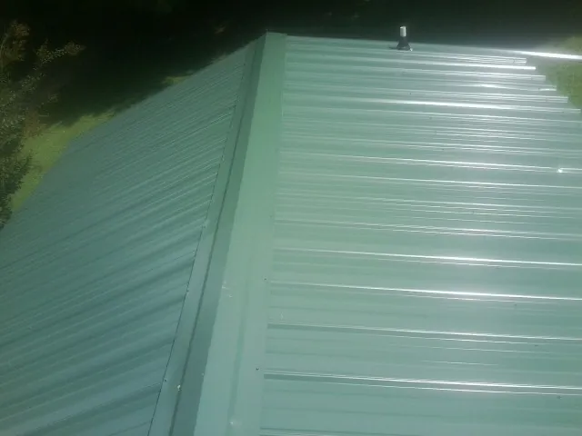 New green metal panels meeting at the ridge of a roof — Flat Roof Repair work by our crew in Rhodesdale