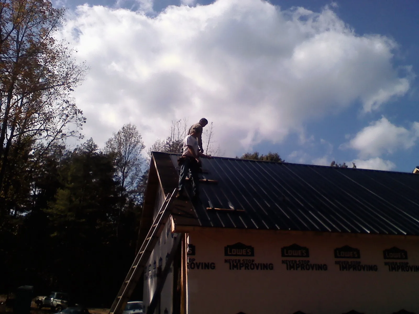 Roofer fastening dark metal panels high against a cloudy sky, from a Roof Inspection job in Rhodesdale