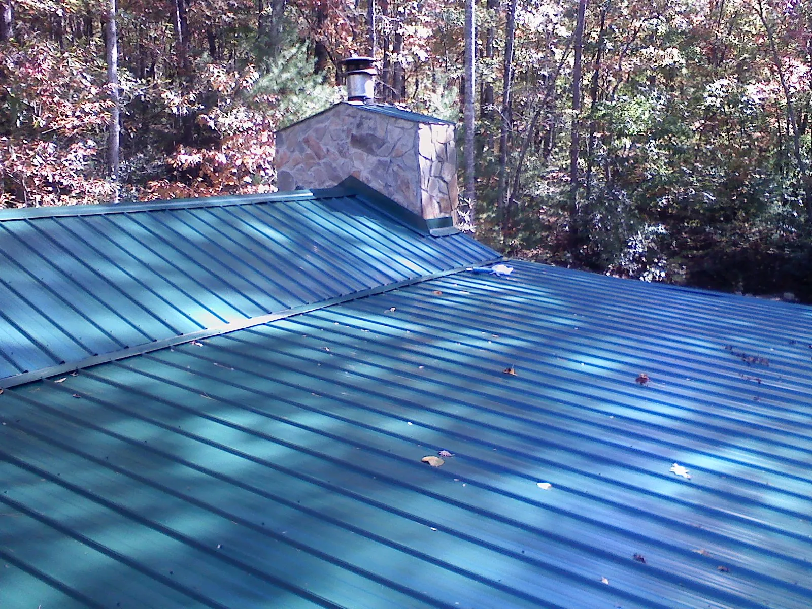 New green metal roof and stone chimney surrounded by autumn woods in Rhodesdale