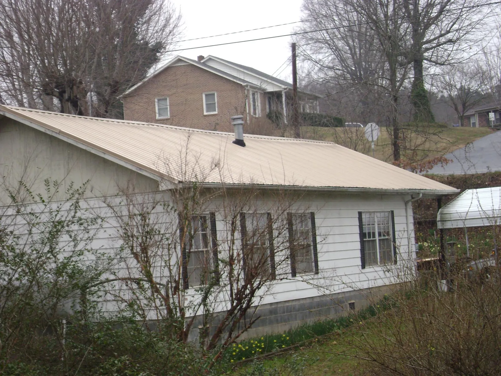 Tan metal roof on a white sided house set into a hillside — Commercial Roofing by Roofing Brothers in Rhodesdale