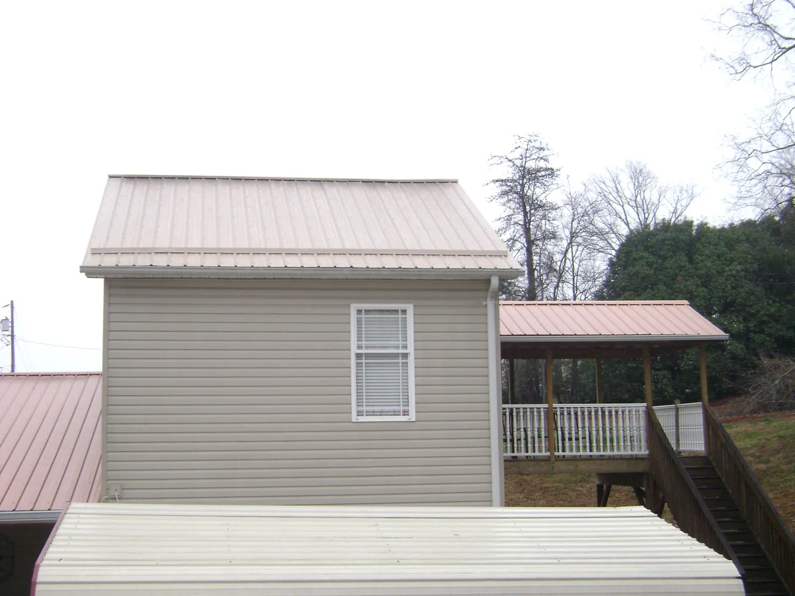 Tan metal roofs on a two story addition and attached porch, from a Roof Replacement job in Rhodesdale